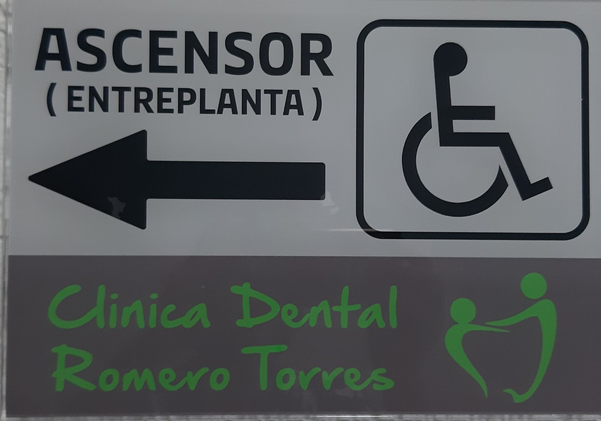 Letrero: Ascensor (entrepiso) con flecha y símbolo de silla de ruedas, además de “Clínica Dental Romero Torres” y un ícono de una persona ayudando a otra.