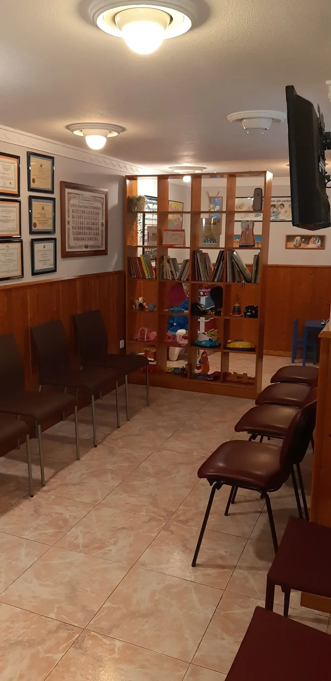Sala de espera con sillas, premios, vitrina y luces de techo. Suelo de baldosas y paredes revestidas de madera.