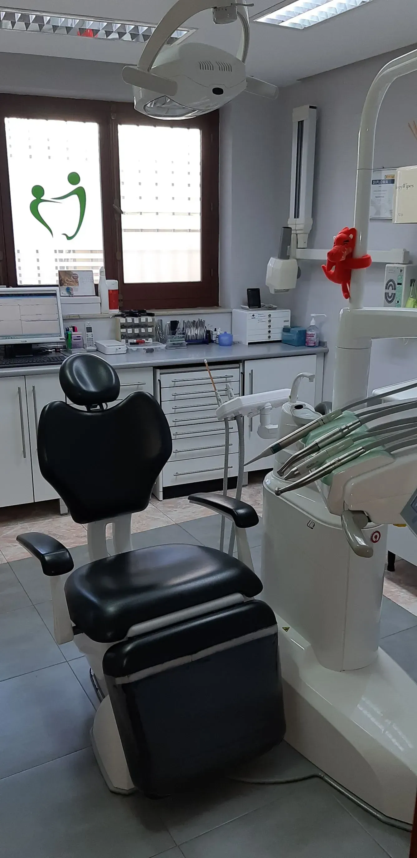 Un consultorio dental con una silla negra, equipamiento y una ventana con un logo.