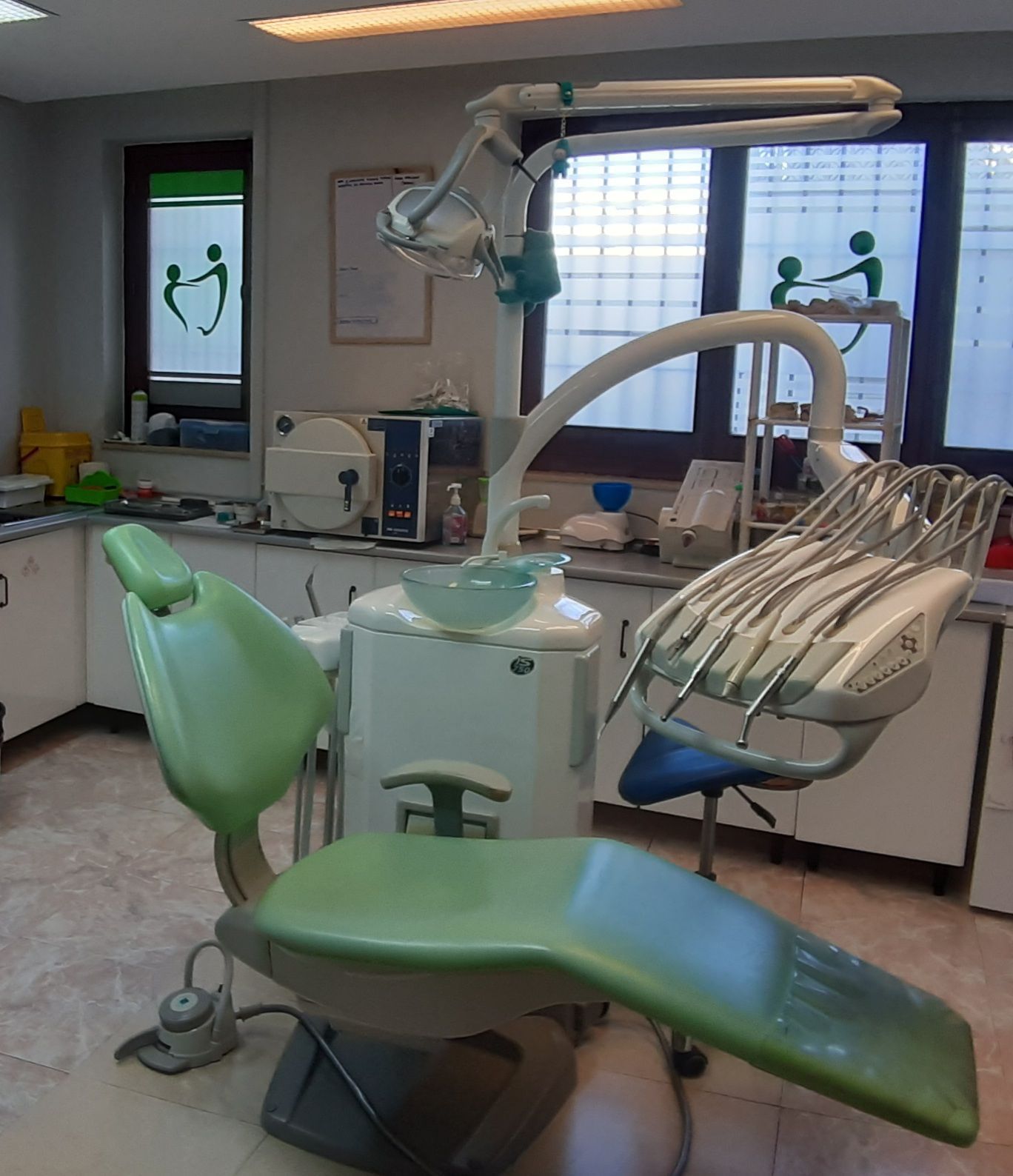 Sillón dental verde en el consultorio de un dentista con herramientas y equipos dentales visibles.