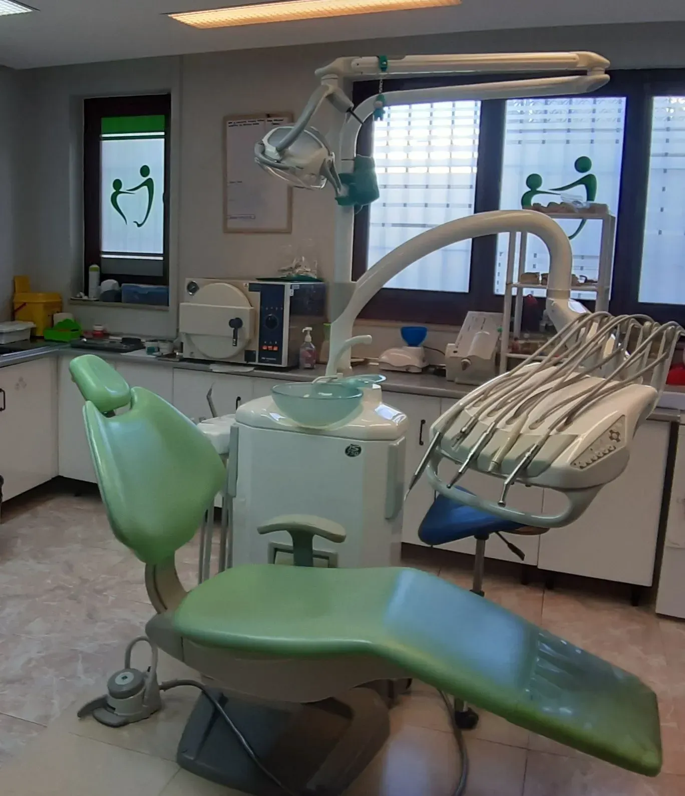 Sillón dental verde en el consultorio de un dentista con herramientas y equipos dentales visibles.