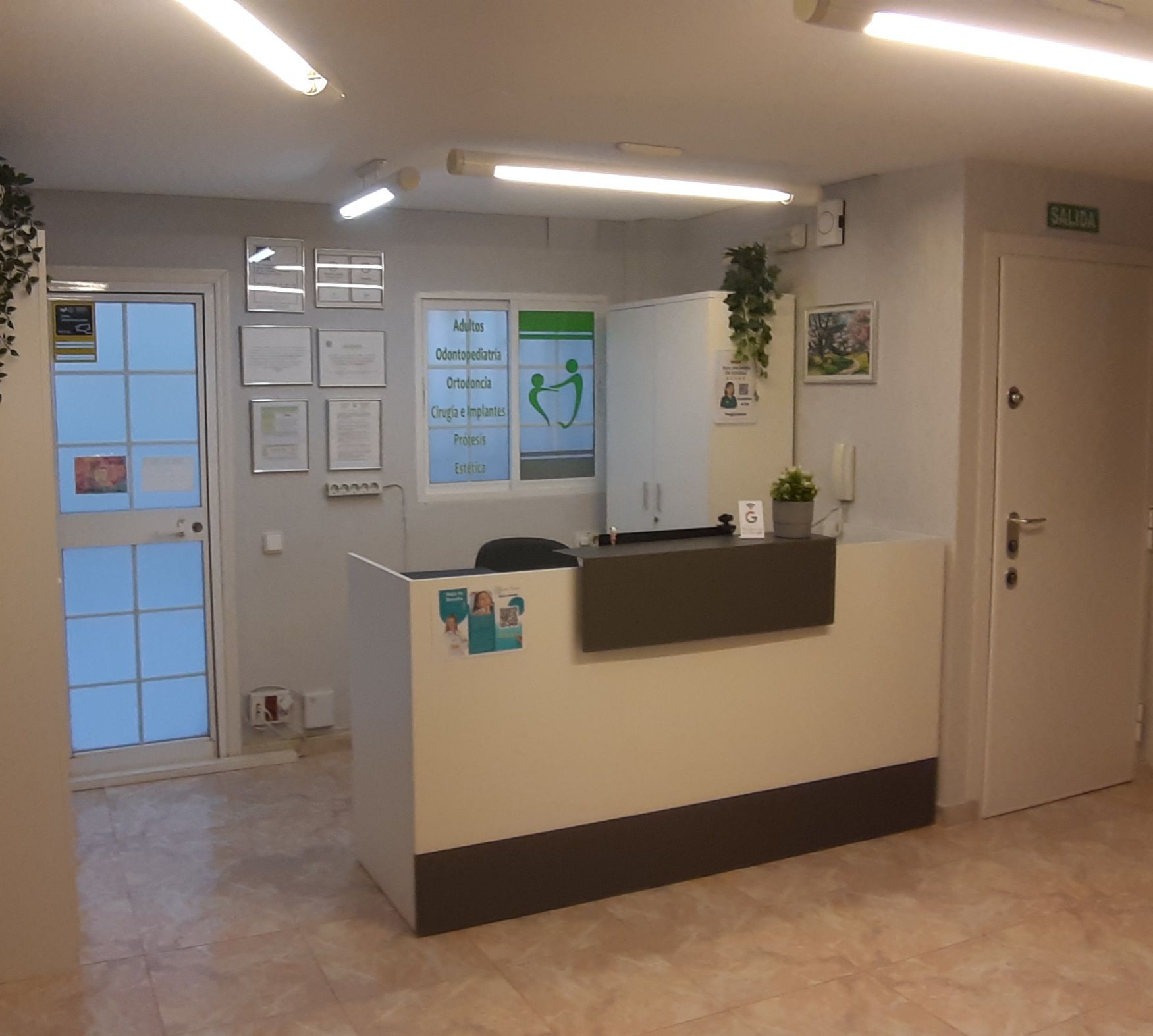 Recepción con escritorio blanco, puerta y letrero. Bien iluminada.
