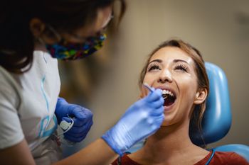 Dentista limpiando con hilo dental a un paciente. El paciente sonríe ampliamente y mira hacia arriba. El dentista usa mascarilla y guantes en el consultorio.