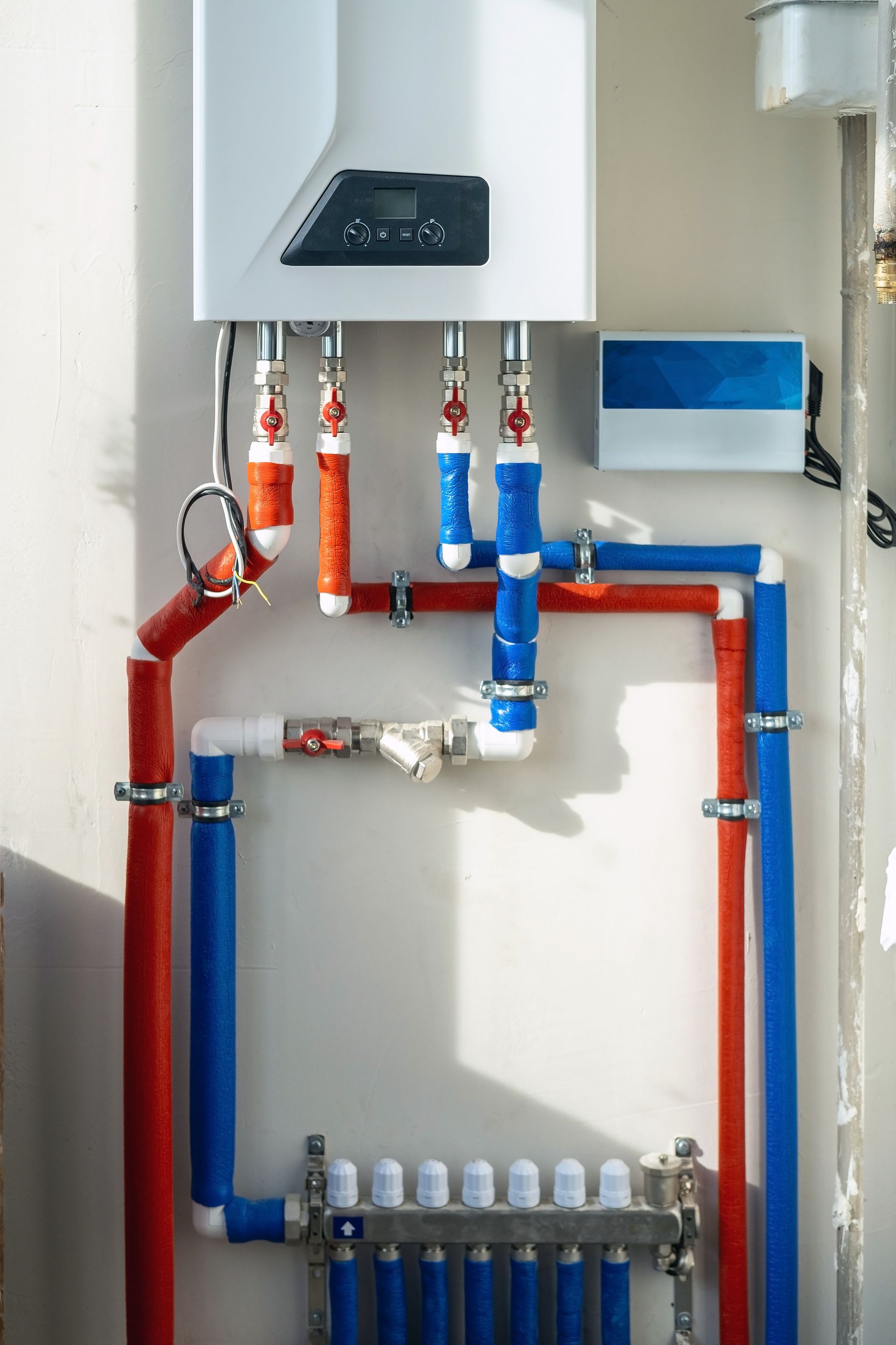 Mur blanc avec un système de chauffage, composé de tuyaux rouges et bleus reliés à un boîtier blanc doté d'un affichage numérique.