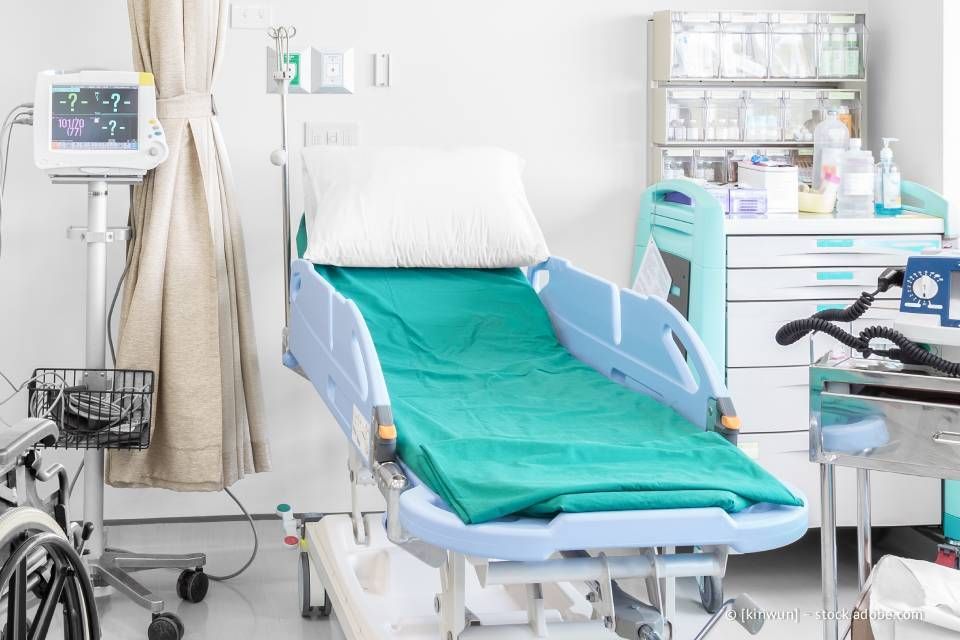 Krankenhausbett mit blaugrünem Laken, Monitor, Vorhang und Zubehör.