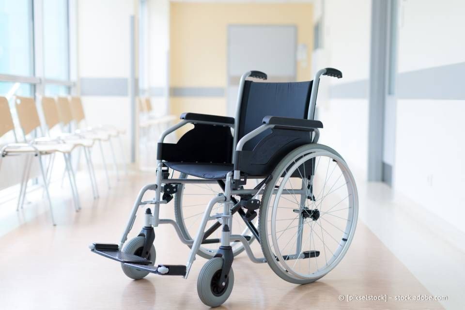 Rollstuhl in einem Krankenhausflur mit Stühlen, was auf eine medizinische Umgebung hindeutet.