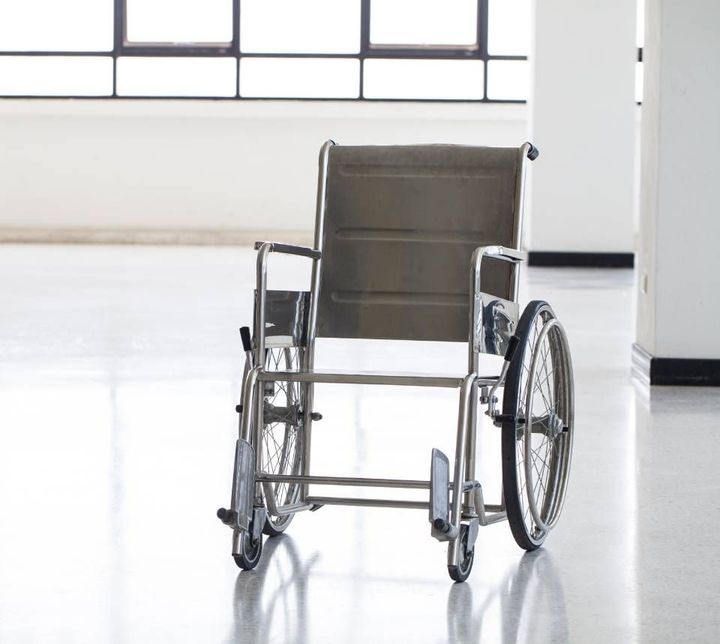 Rollstuhl in einem hellen, leeren Flur mit großen Fenstern.