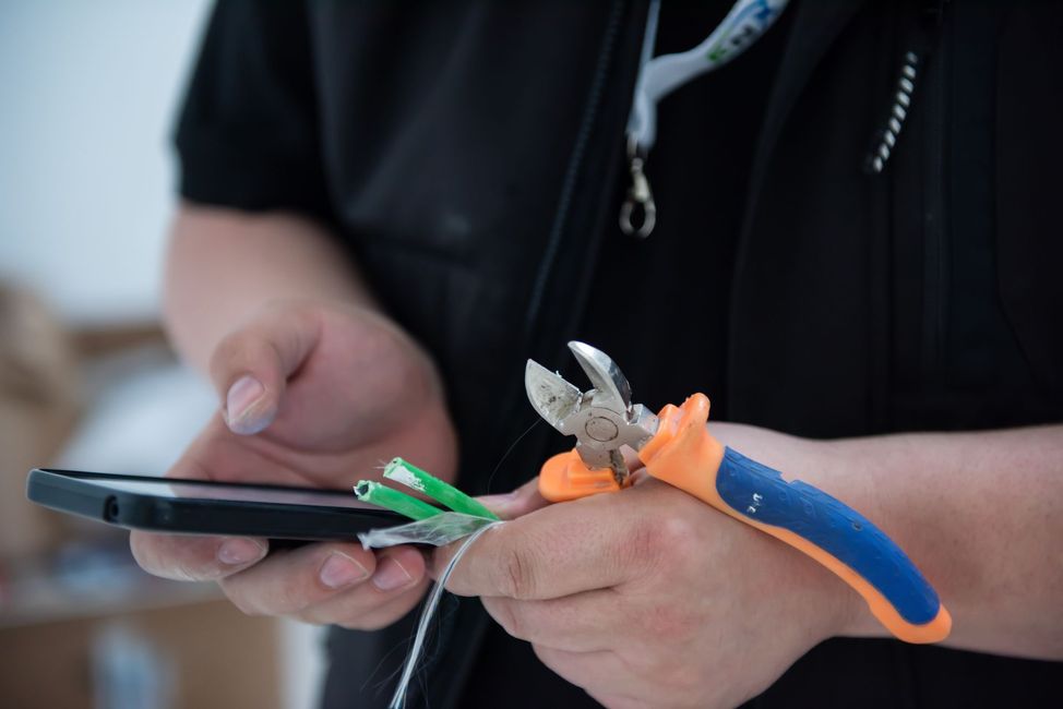 Mains tenant un câble électrique dénudé, une pince et un téléphone