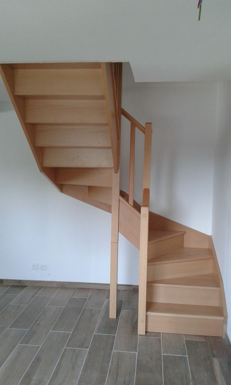 Escalier en bois aux lignes courbes, installé dans une pièce aux sols en bois clair et aux murs blancs.