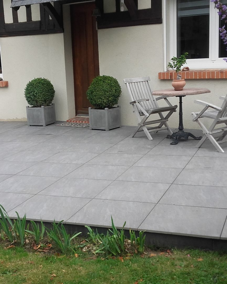 Terrasse grise avec plantes en pot, meubles en bois et porte d'entrée.