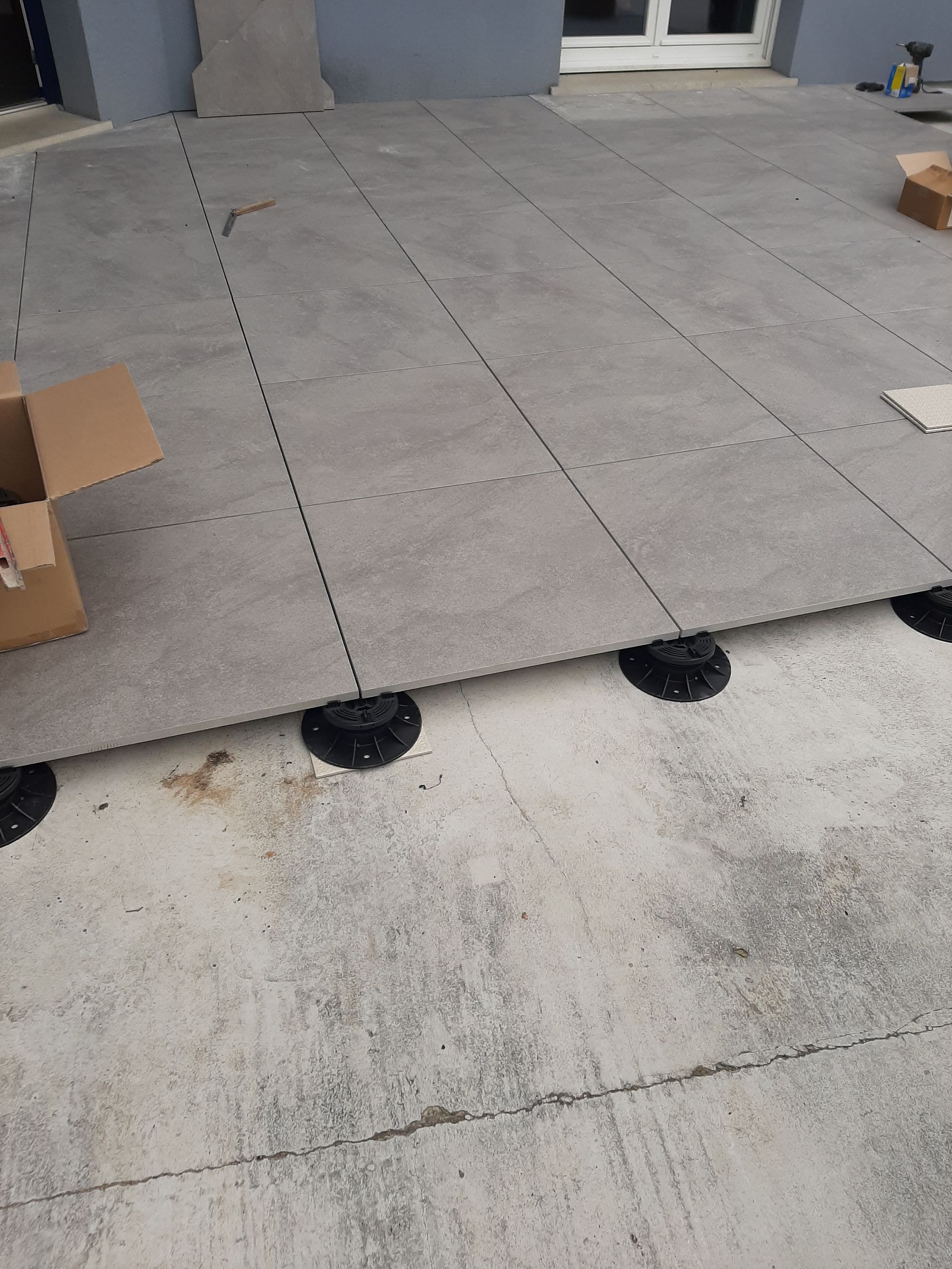 Pose de dalles de pierre grise sur des socles noirs au-dessus d'une terrasse en béton.
