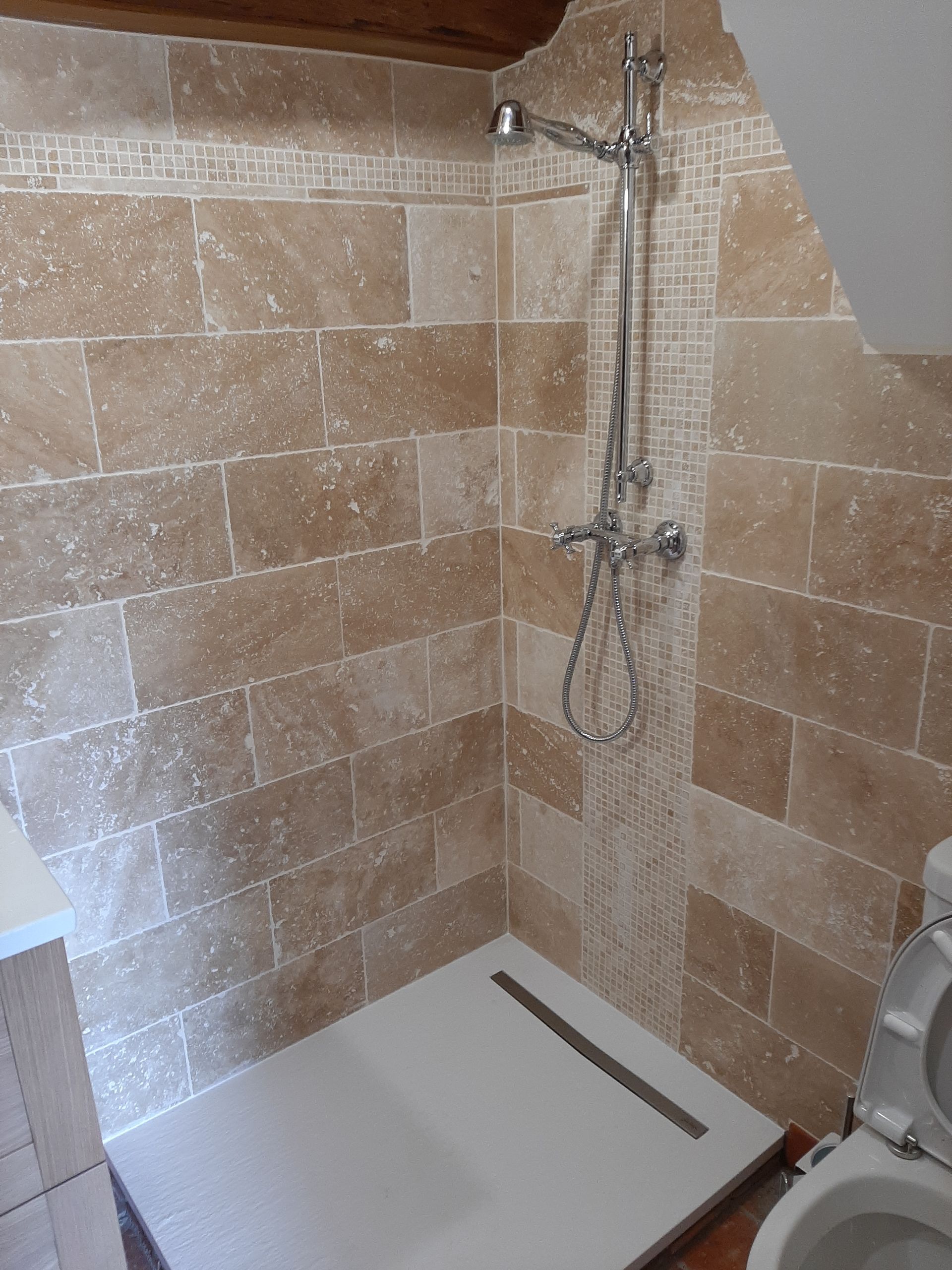 Une douche avec mur carrelé de carreaux de pierre beige et bordure en mosaïque.