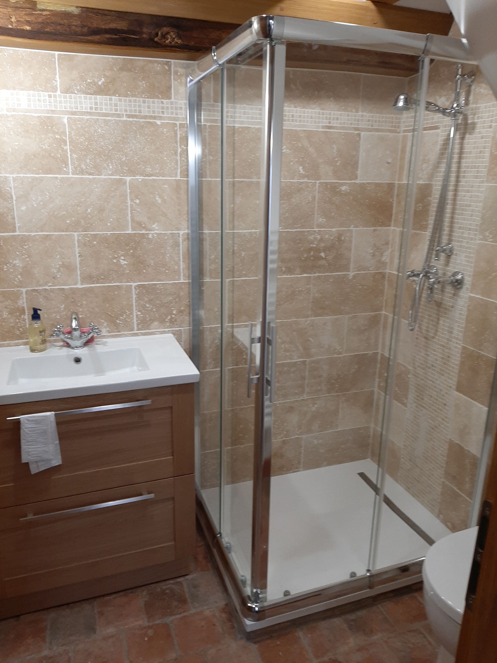 Salle de bains avec douche d'angle, meuble-lavabo en bois et murs carrelés beiges.