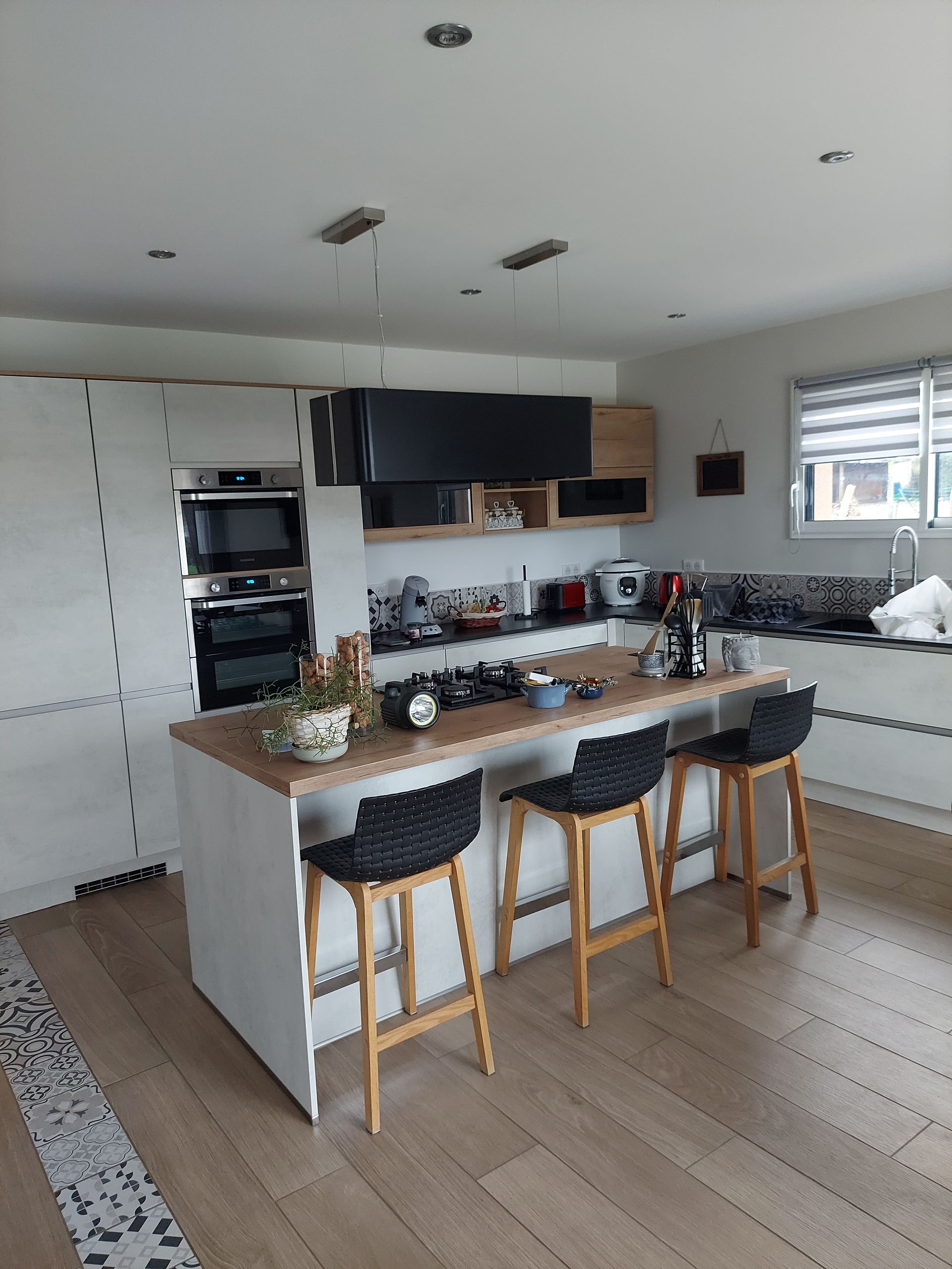 Cuisine moderne avec îlot central, placards blancs et trois tabourets de bar.