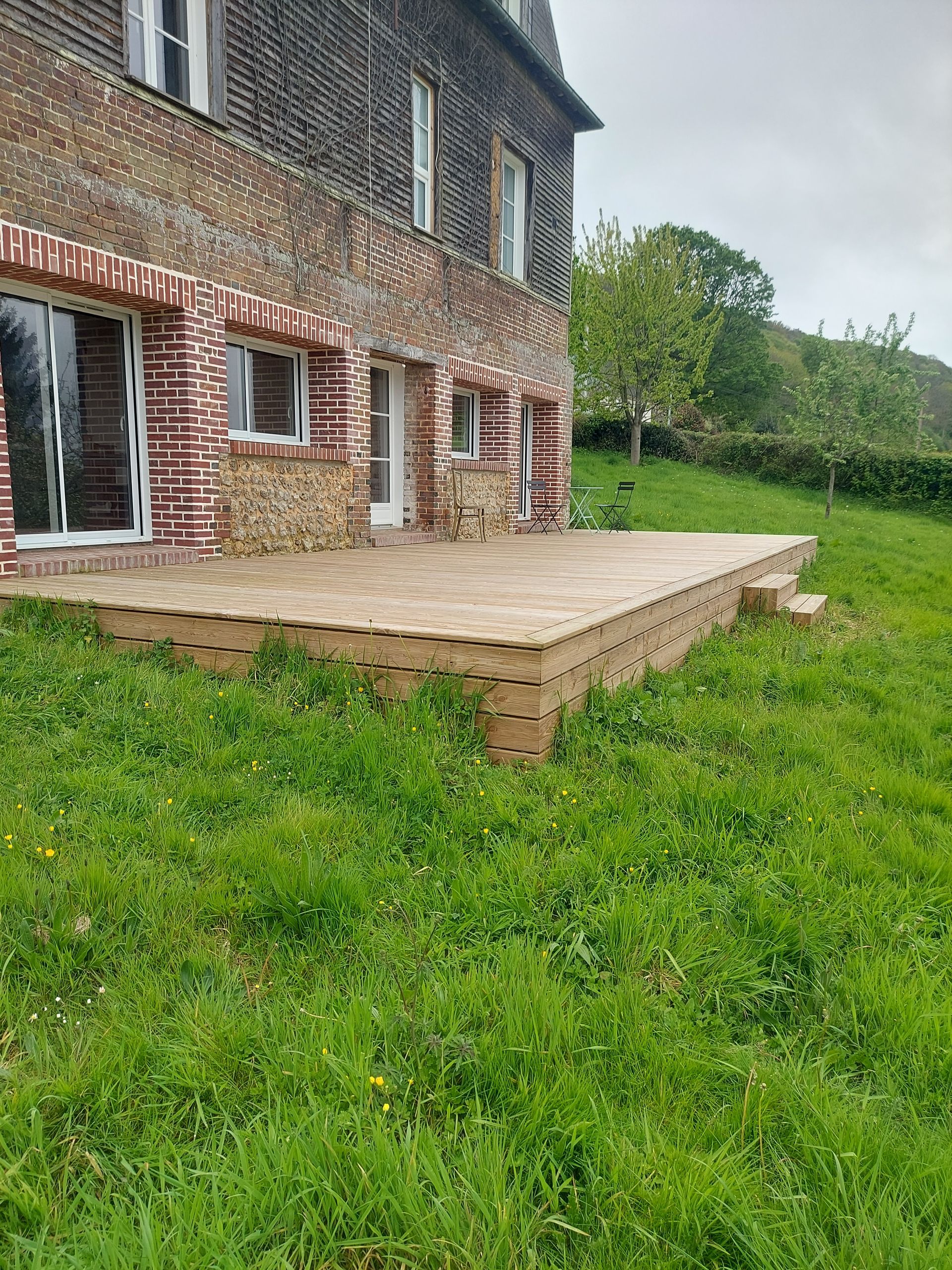 Terrasse en bois à l'extérieur d'un bâtiment en briques ; pelouse verte tout autour.