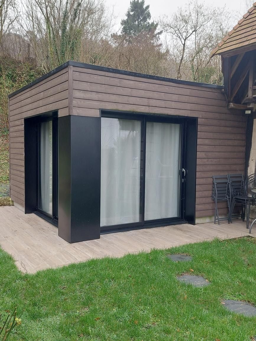 Abri de jardin moderne aux parois brunes, avec des finitions noires et de grandes portes vitrées, terrasse en bois.
