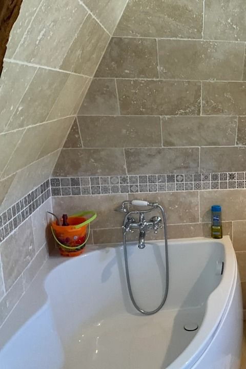 Baignoire avec murs carrelés beiges, bordure en mosaïque et robinet avec douchette.