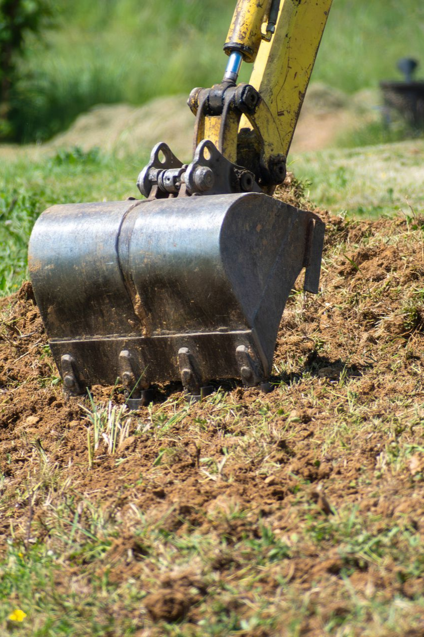 Godet jaune d'une excavatrice ramassant de la terre dans un champ herbeux.