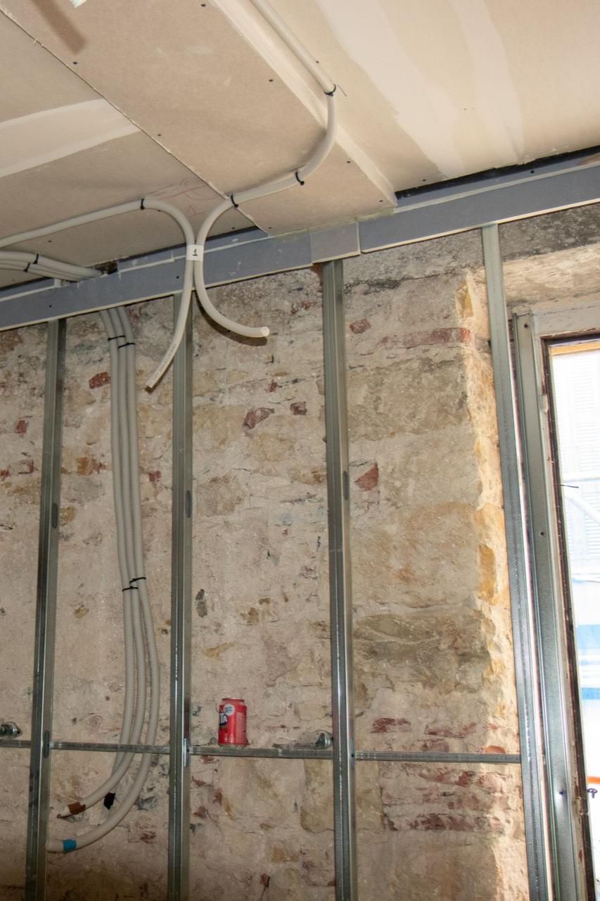 Construction intérieure : ossature métallique contre un mur de briques patiné, avec conduits électriques apparents.