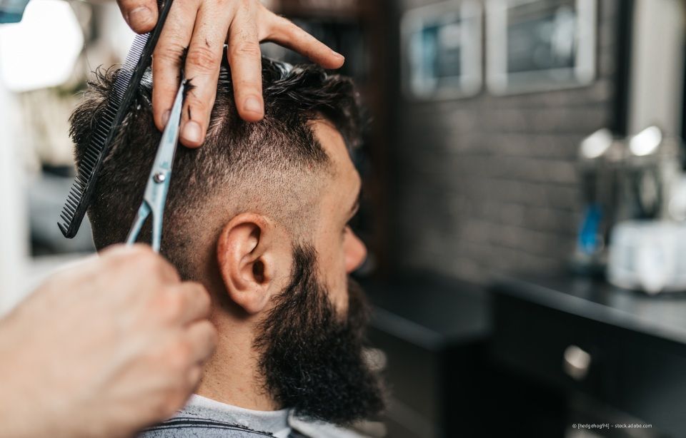 Ein Barbier stutzt einem Mann in einem Friseursalon Bart und Haare mit einer Haarschneidemaschine.