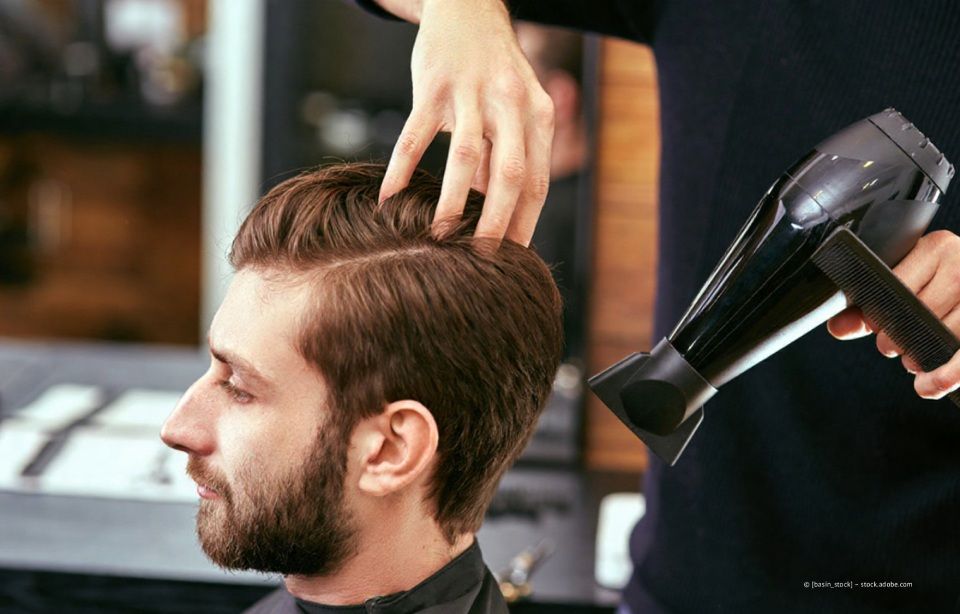 Ein Friseur föhnt einem Mann im Salon die Haare.