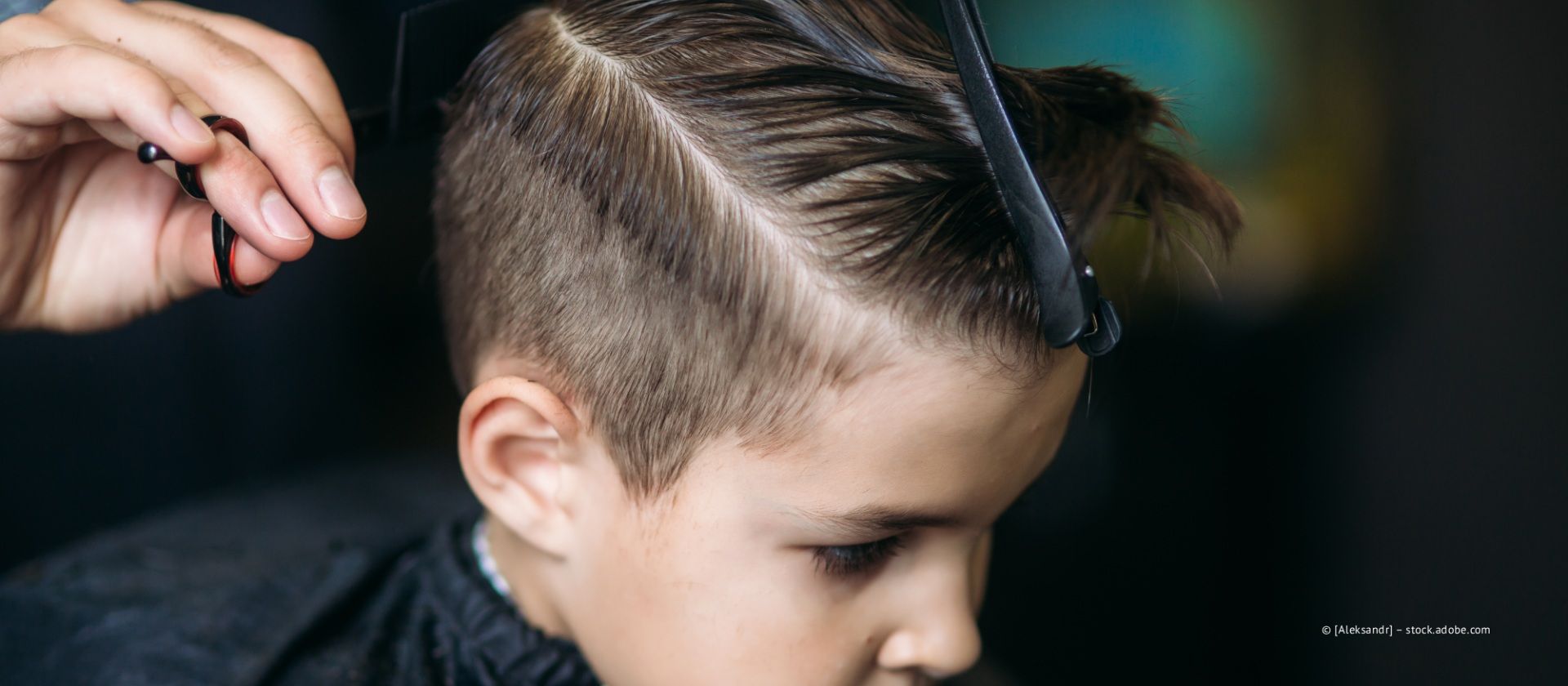 Die Hand eines Barbiers hält Schere und Kamm, während er einem Menschen die Haare schneidet.