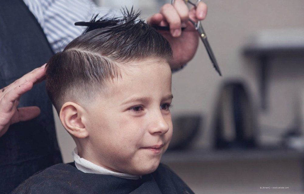 Kind beim Haareschneiden mit einer Schere, lächelnd im Friseurstuhl