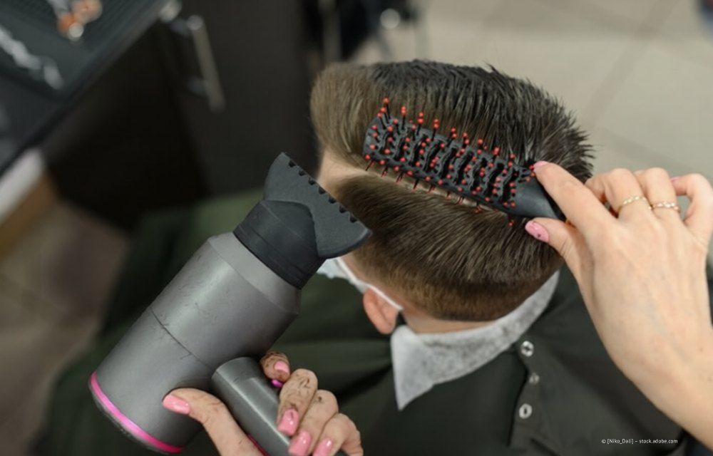 Eine Friseurin föhnt einer Kundin in einem Salon die kurzen Haare mit einer Rundbürste.
