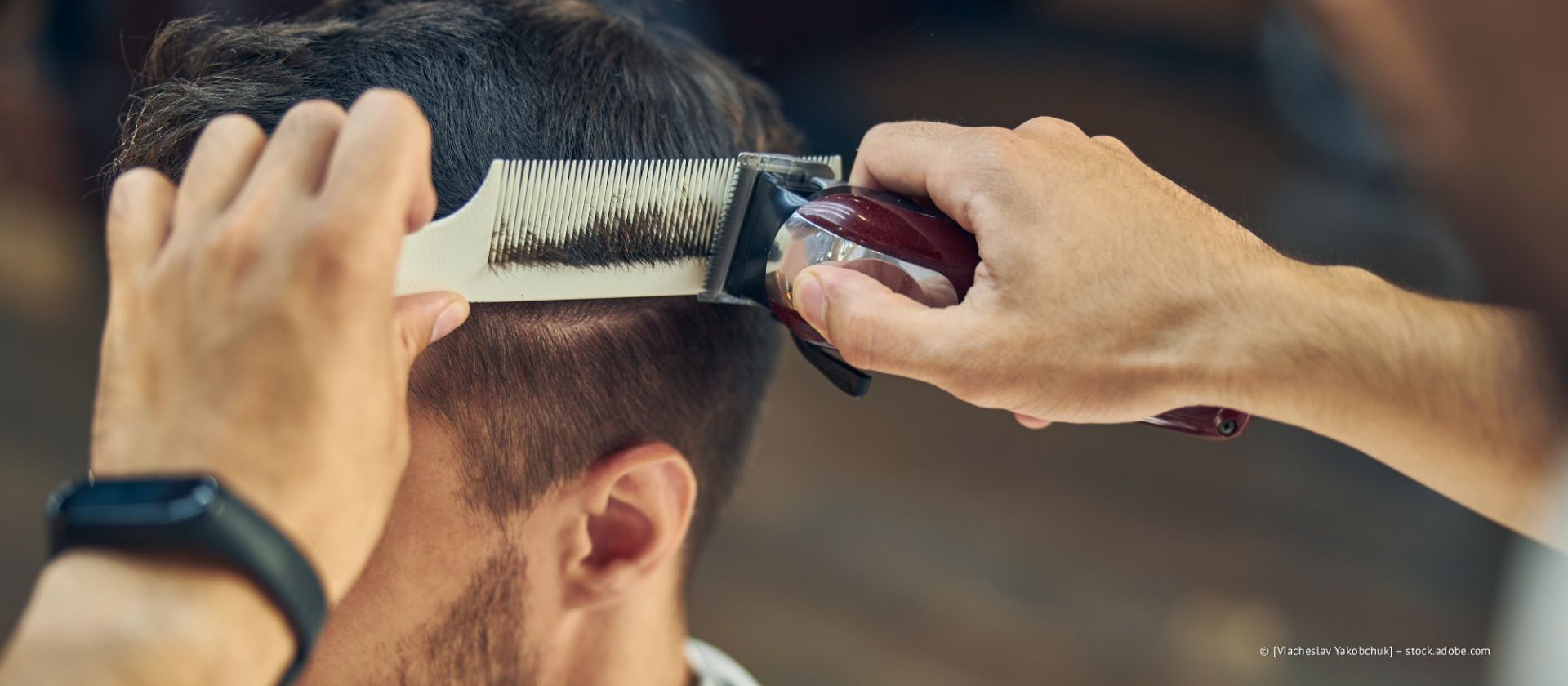 Ein Barbier benutzt einen Kamm und eine elektrische Haarschneidemaschine, um die Haare an den Seiten des Kopfes eines Kunden zu trimmen.