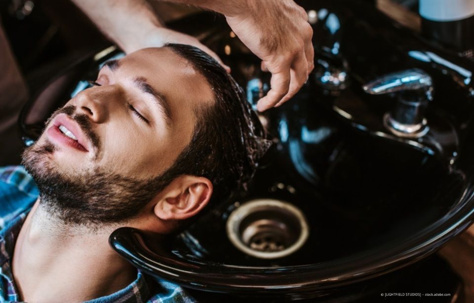 Ein Mann liegt an einem Waschbecken im Friseursalon, während ihm ein Stylist die Haare wäscht.