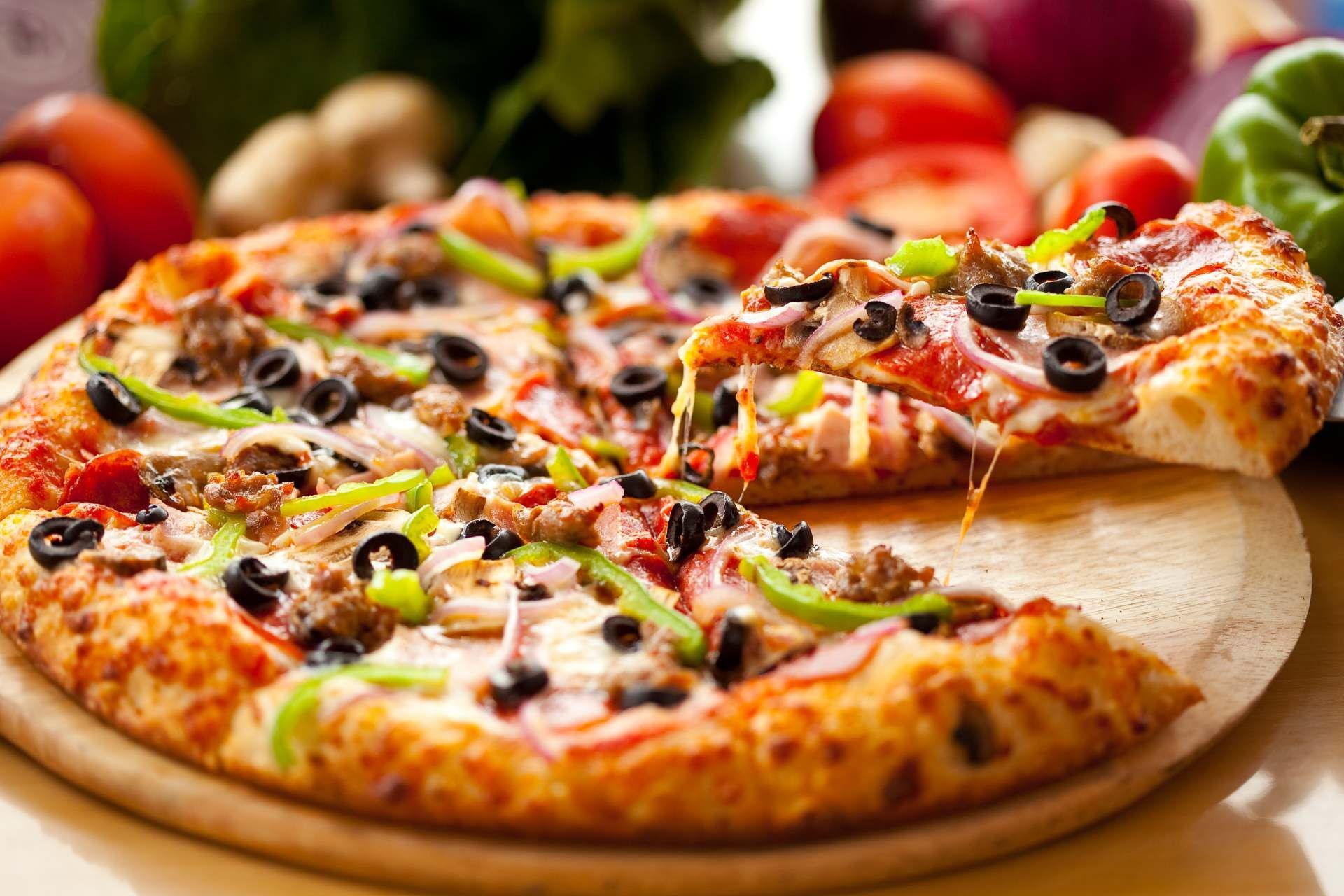Auf einem Holzbrett steht eine Pizza mit einem Stück genommen.