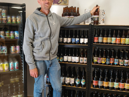 Une personne se tient dans l'allée d'un magasin de boissons, tenant une bouteille à côté des rayons de vins et de boissons.