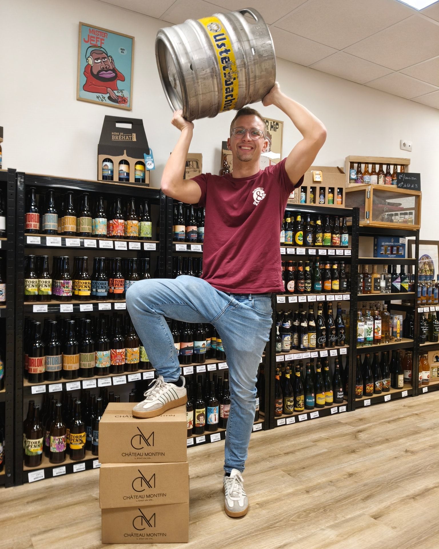 Une personne en équilibre sur des caisses dans un magasin d'alcools, soulevant un grand fût de bière au-dessus de sa tête.
