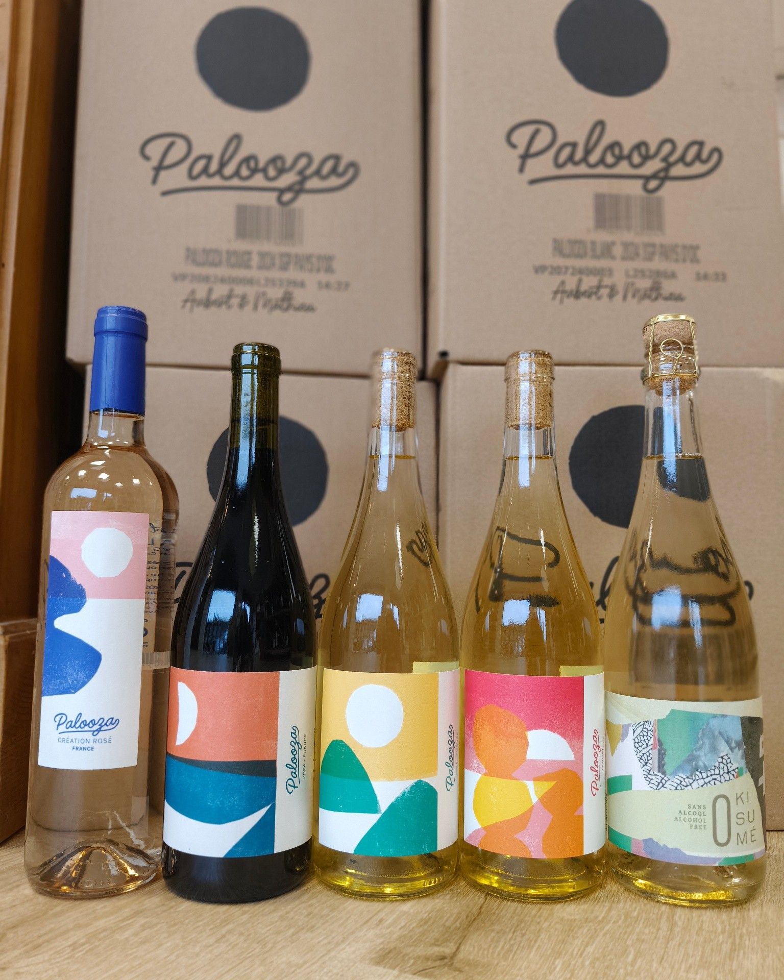 Cinq bouteilles de vin colorées sont présentées devant des boîtes estampillées Palooza.