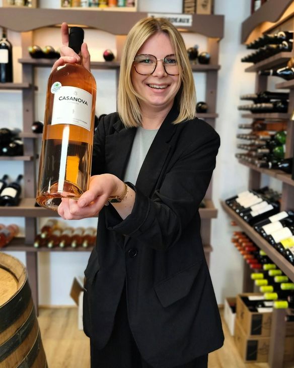 Une personne souriante dans une cave à vin tient une bouteille de rosé.