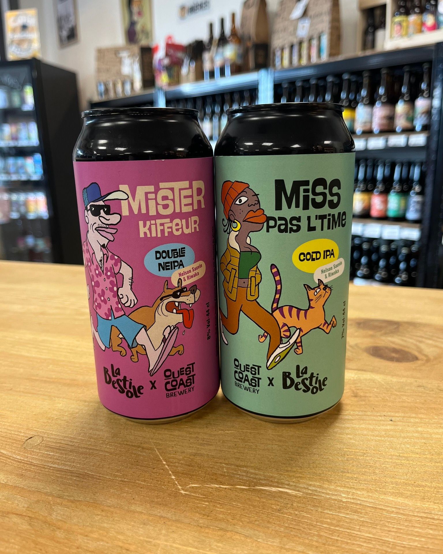 Deux canettes de bière colorées, avec des étiquettes roses et vertes à motifs de dessins animés, posées sur une table en bois dans un magasin.