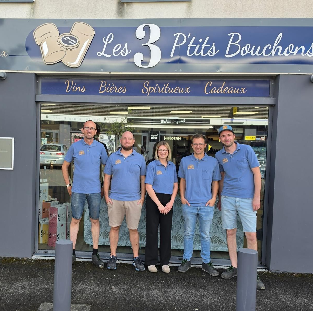 Cinq employés en chemises bleues se tiennent devant l'entrée du magasin Les 3 P'tits Bouchons
