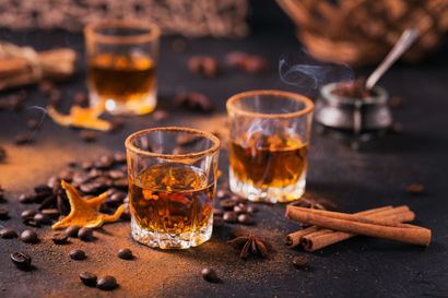 Verres de boisson ambrée épicée avec des bâtonnets de cannelle et de l'anis étoilé sur une table sombre