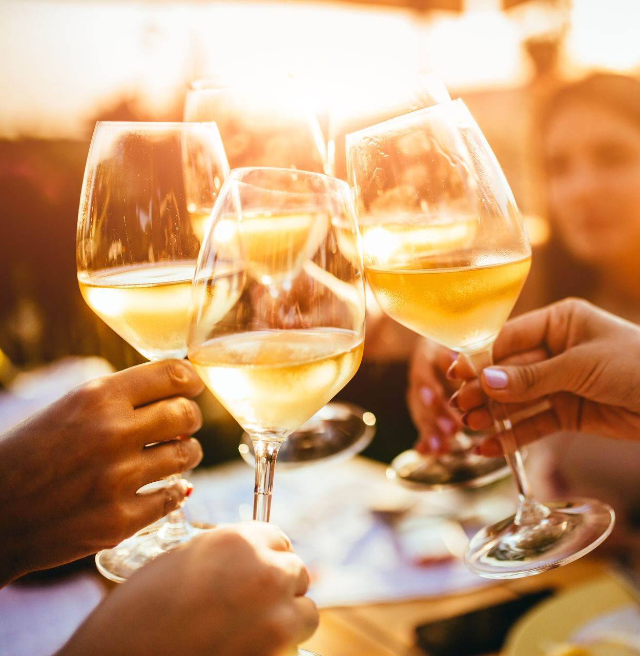 Des amis trinquent avec du vin blanc lors d'un toast ensoleillé en plein air