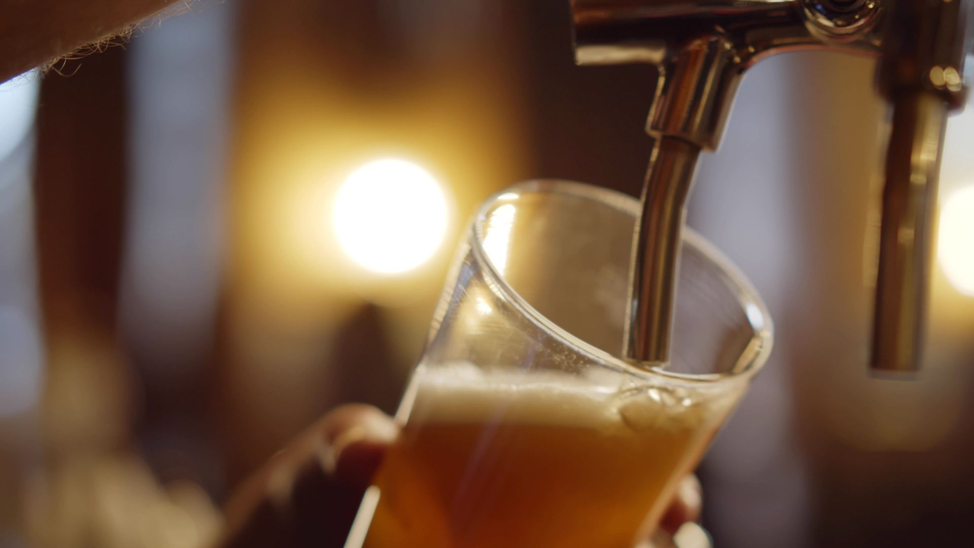 Du café se verse d'une machine dans un verre incliné, avec des lumières bokeh chaudes en arrière-plan.