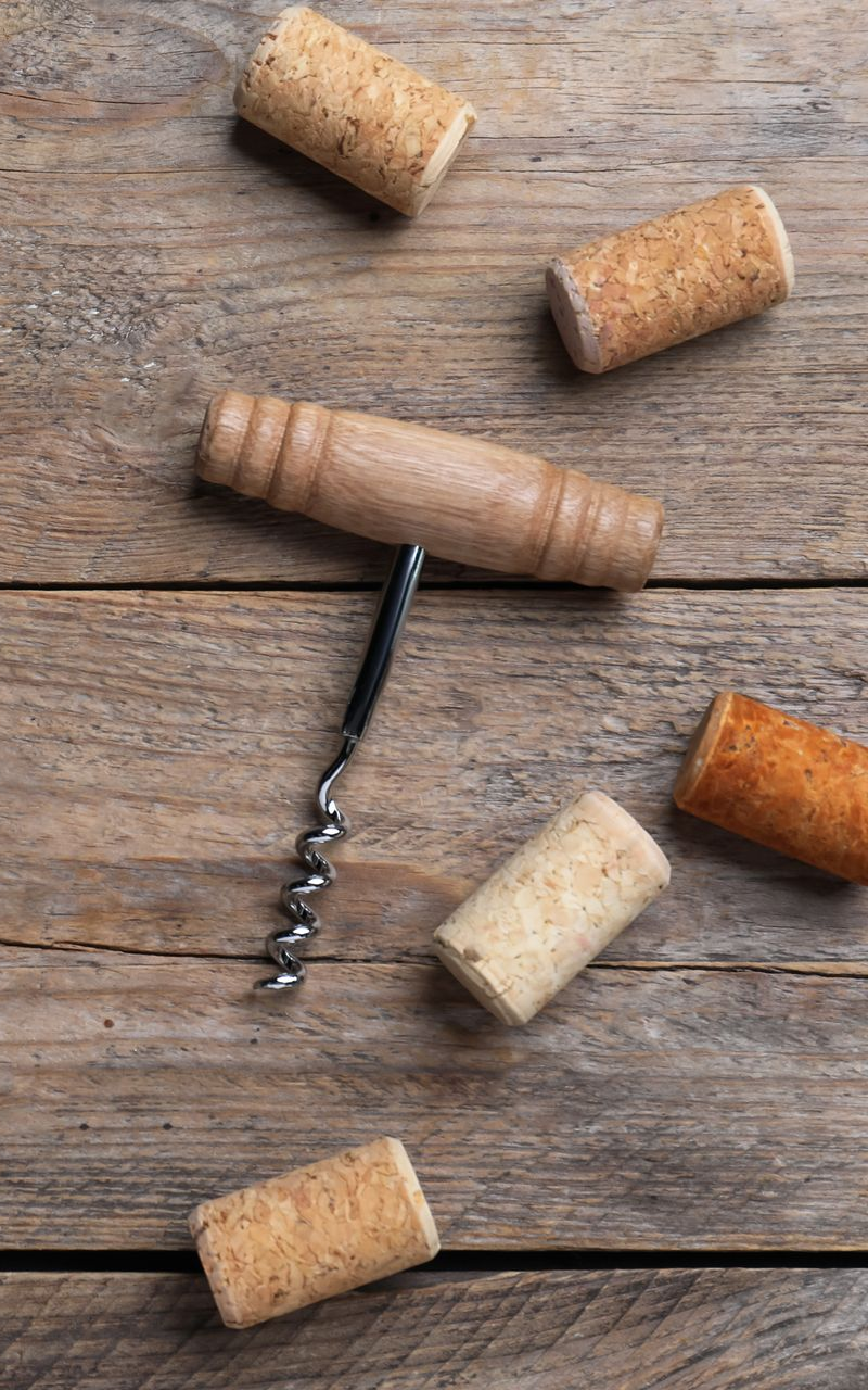 Des bouchons de vin et un tire-bouchon sur une table en bois patiné, disposés comme une simple nature morte.