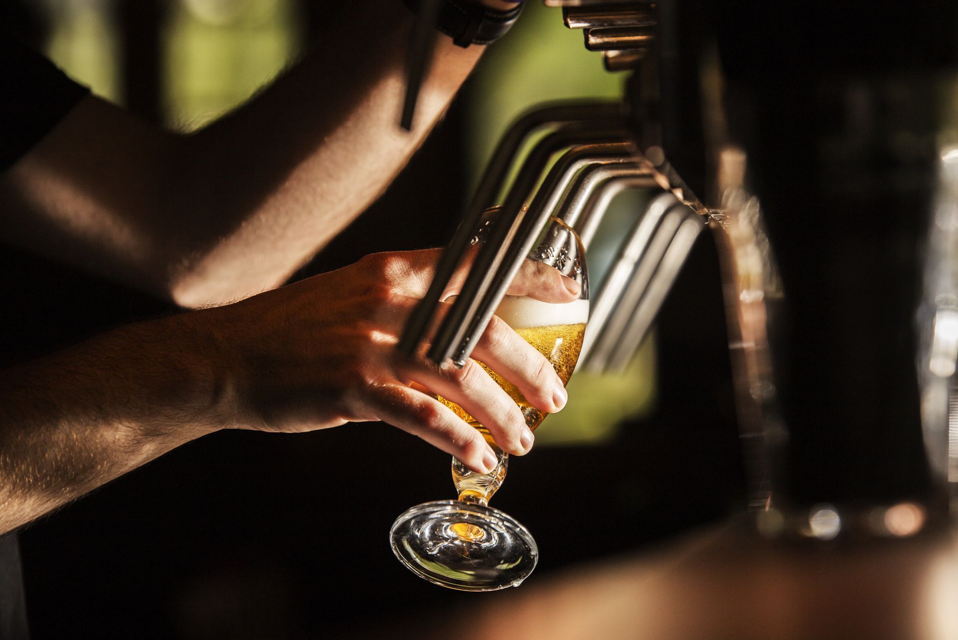 Des mains versent une boisson pâle dans un verre à pied dans un bar à la lumière tamisée.