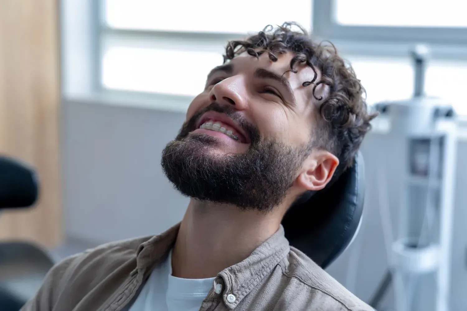 Una persona sonriente, con cabello rizado y barba, se recuesta en una silla en un consultorio médico o dental.