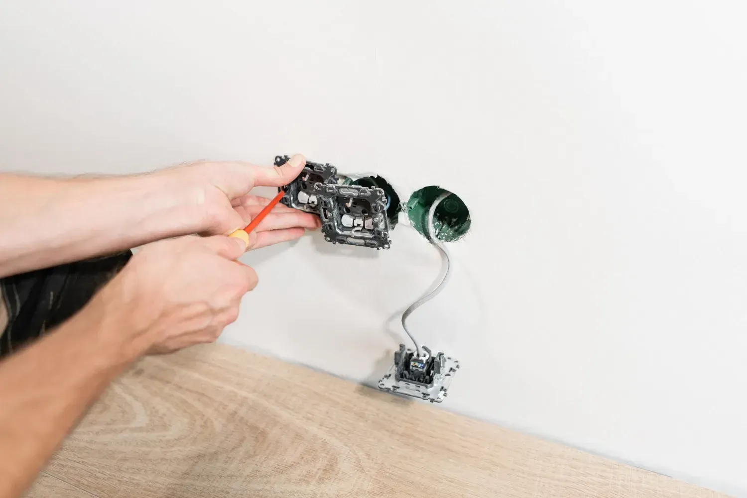 Una persona utiliza un destornillador de mango rojo para instalar componentes eléctricos.