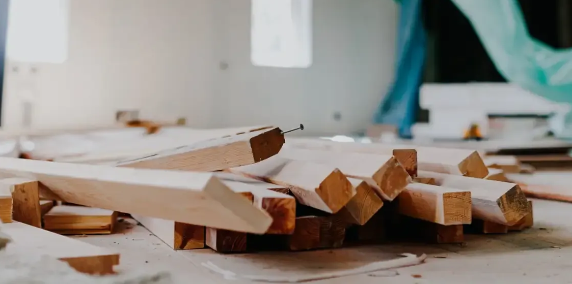 Montones de tablones de madera de color claro y escombros de construcción esparcidos por el suelo de una habitación en obras.
