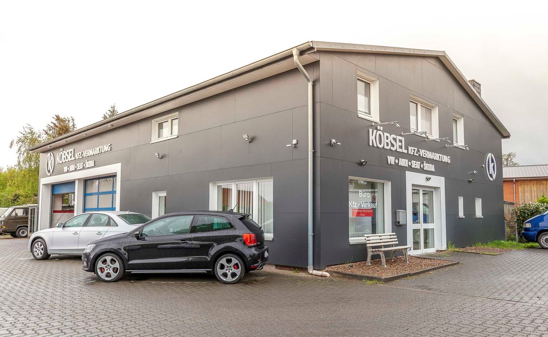 Graues Geschäftsgebäude mit weißen Zierelementen und davor geparkten Autos