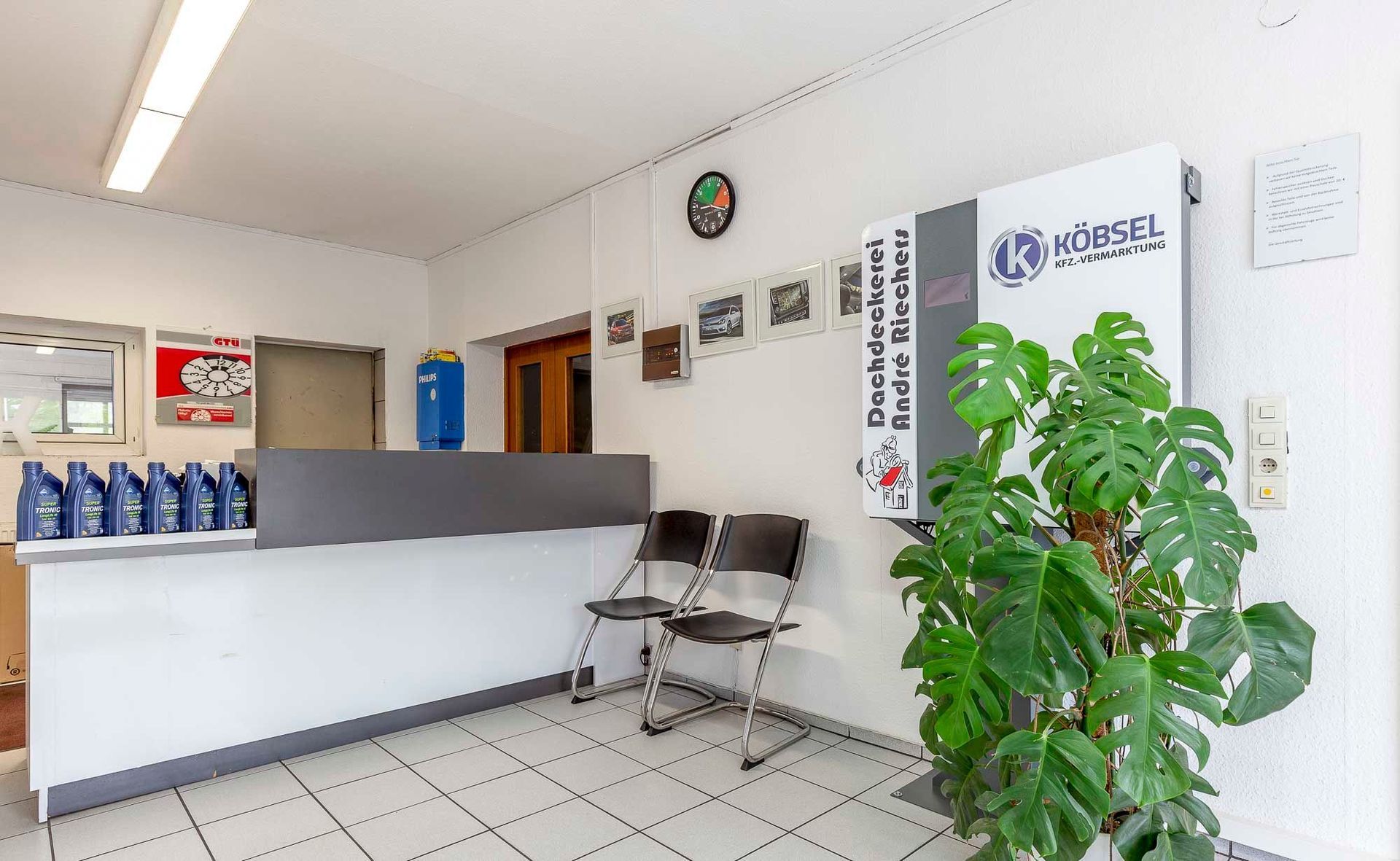 Helle Lobby mit Theke, Stühlen, Wandschildern und einer Topfpflanze neben dem gefliesten Boden.
