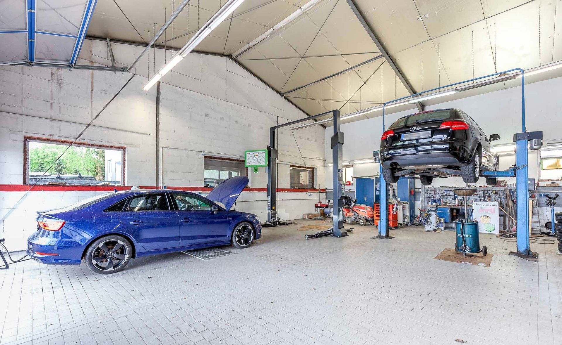 Blauer Sportwagen in einer hellen Autowerkstatt mit Hebebühne und Werkzeug