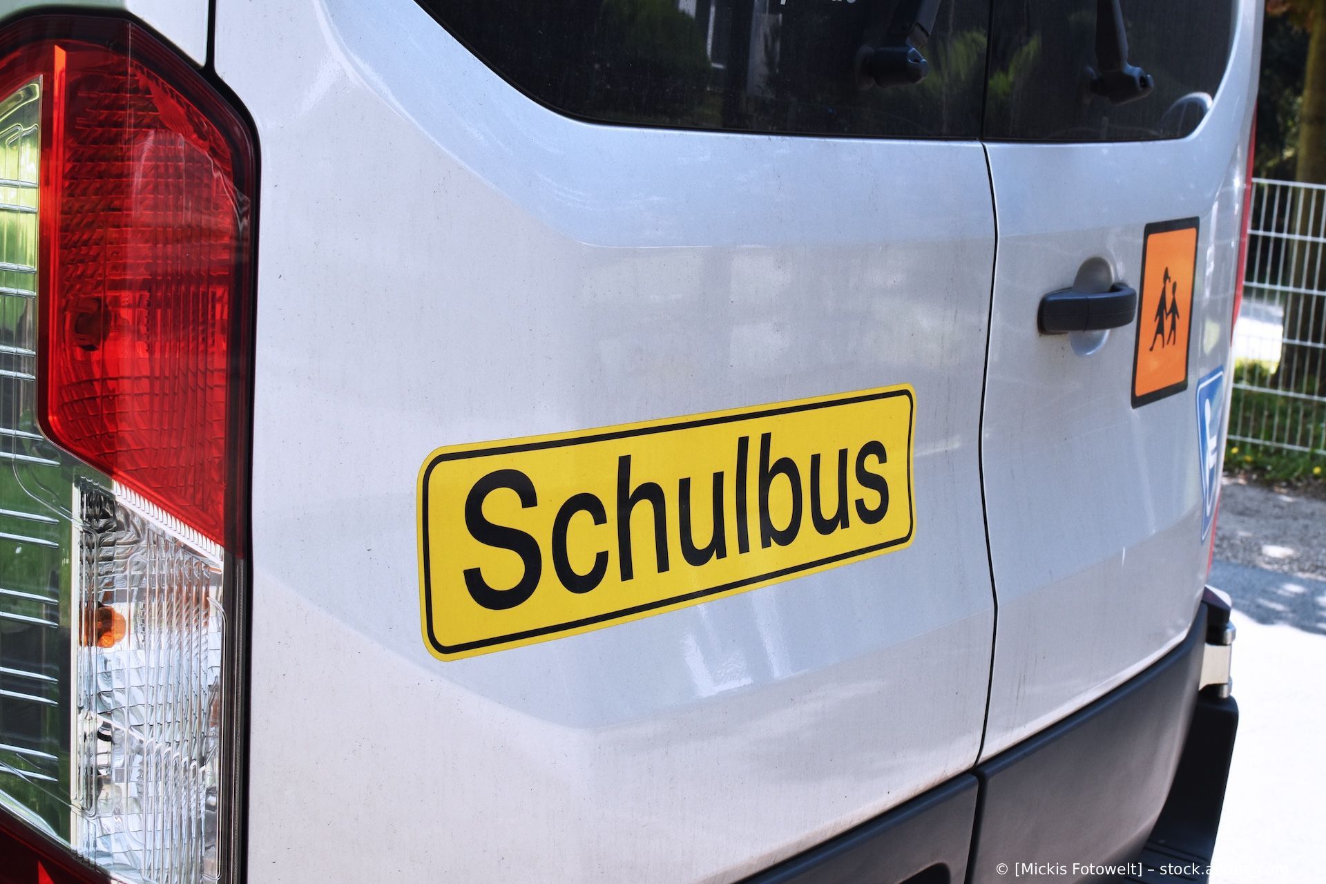 Nahaufnahme eines weißen Lieferwagens mit einem gelben „Schulbus“-Schild an der Seite und einem roten Rücklicht.