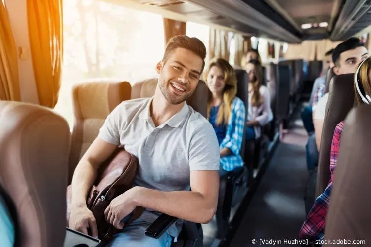 Fahrgäste lächeln in einem Bus, einer hält einen Gitarrenkoffer in der Nähe des Ganges.